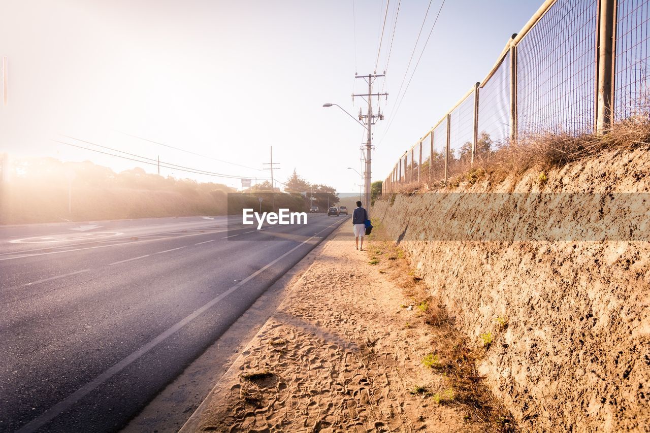 REAR VIEW OF MAN CYCLING ON ROAD