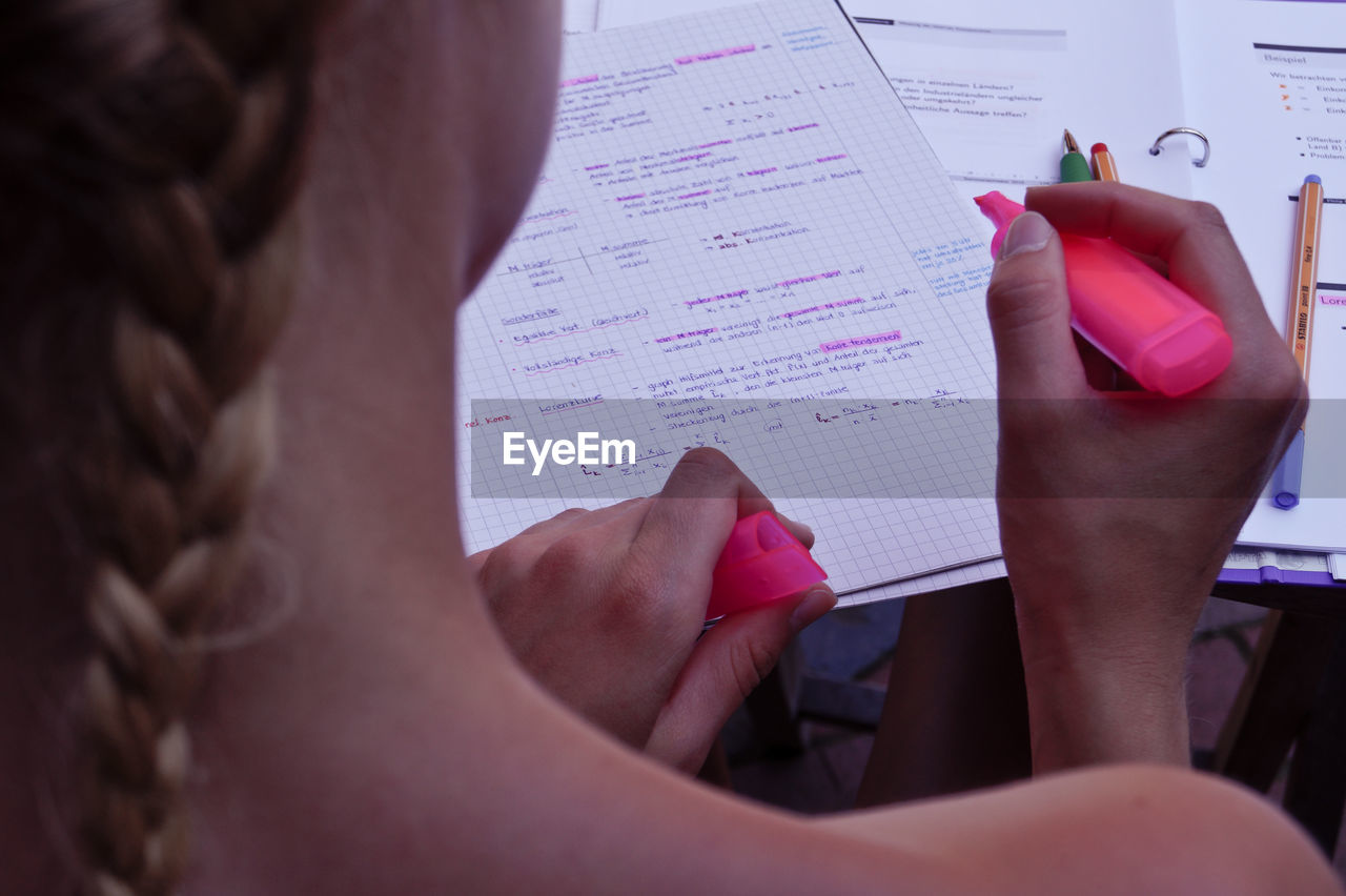 Cropped image of woman holding pink highlighter with documents at table