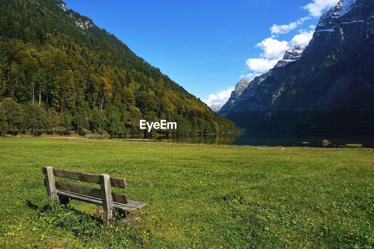 Panoramic view of klontalersee lake with wooden bench in klontal grass valley facing glarus alps