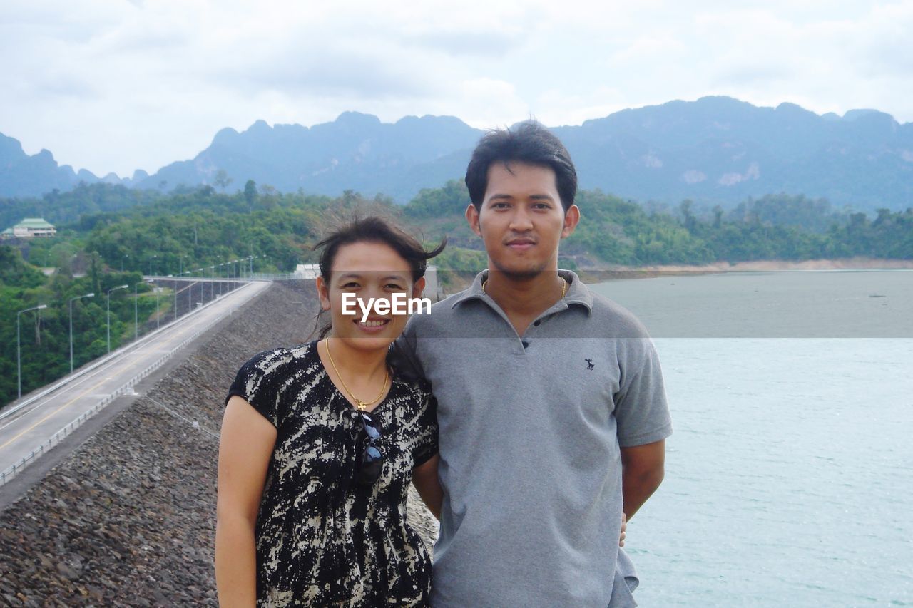 Portrait of smiling couple standing on mountain against lake