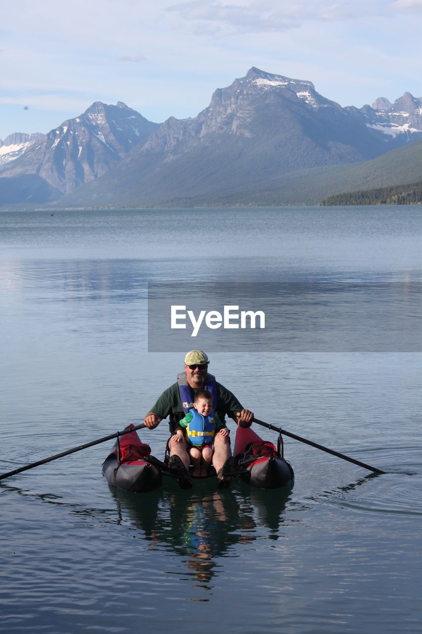 Men with boy in boat on river against mountain