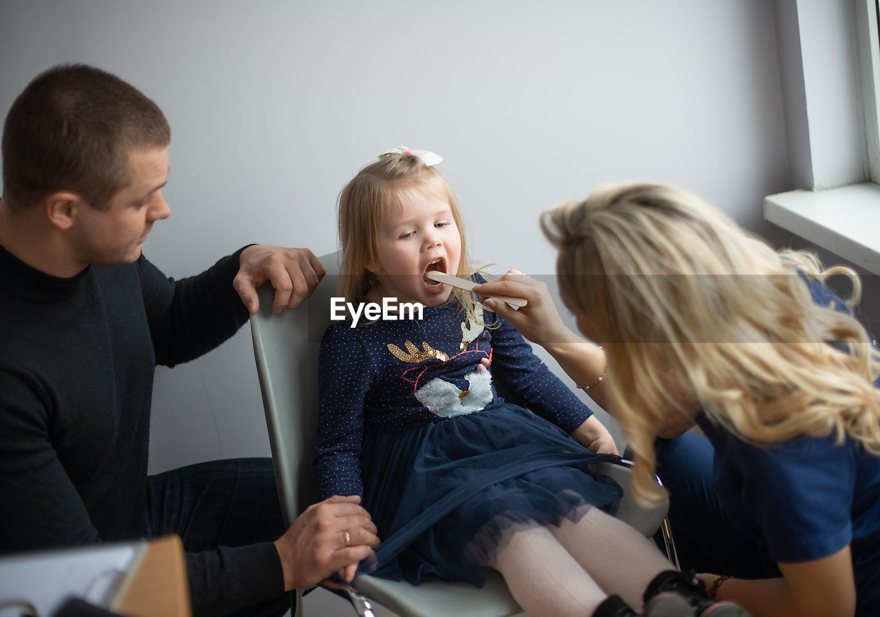 Female doctor examining girl sitting on chair with father in hospital