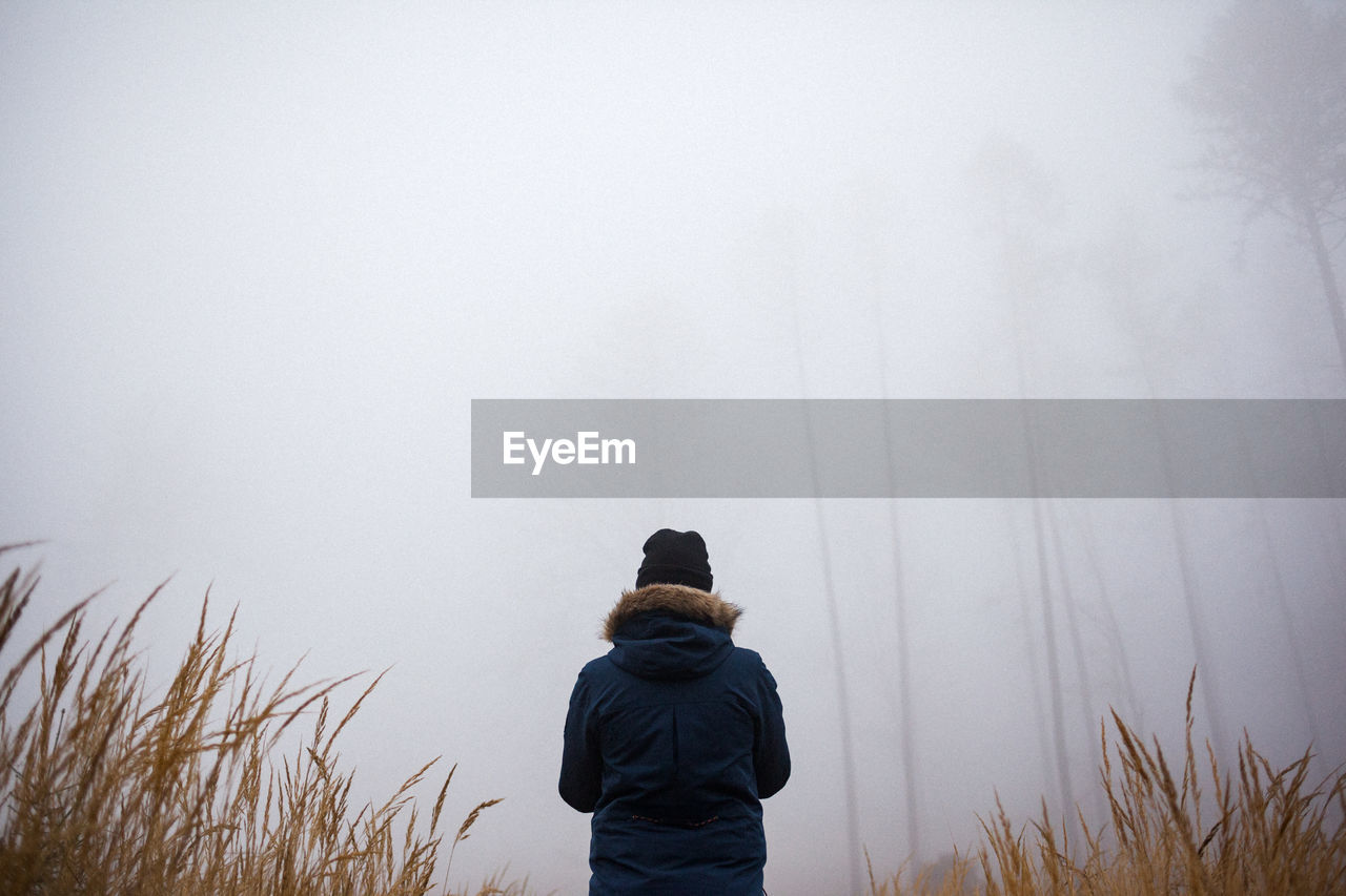 Rear view of woman standing at forest during foggy weather