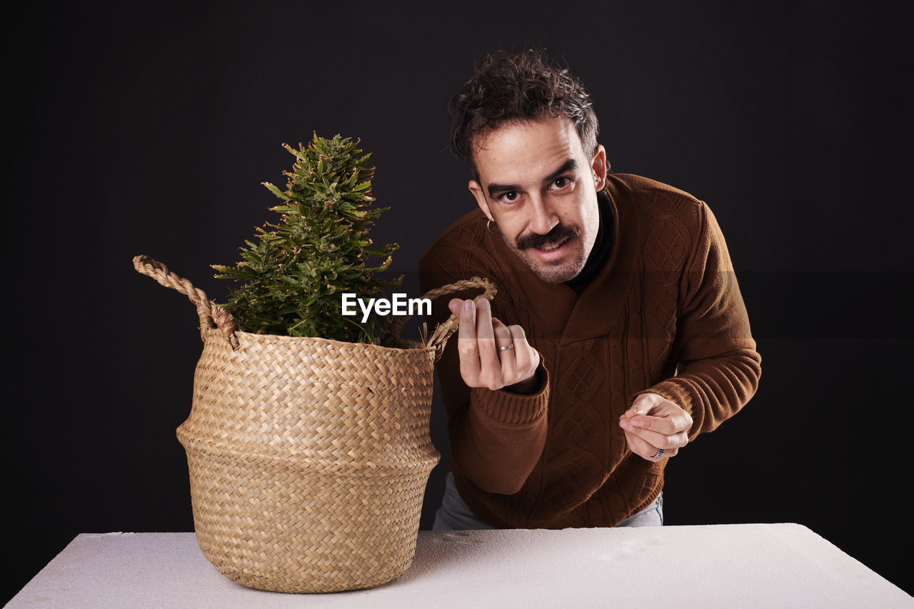 one person, adult, men, person, indoors, studio shot, black background, portrait, plant, picnic basket, clothing, container, business, basket, flowerpot, young adult, beard, front view, emotion, lifestyles, business finance and industry, holding, facial hair