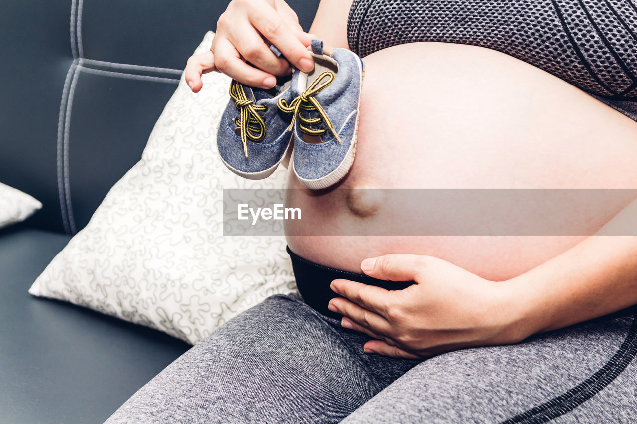 Midsection of pregnant woman holding baby booties while sitting on sofa at home