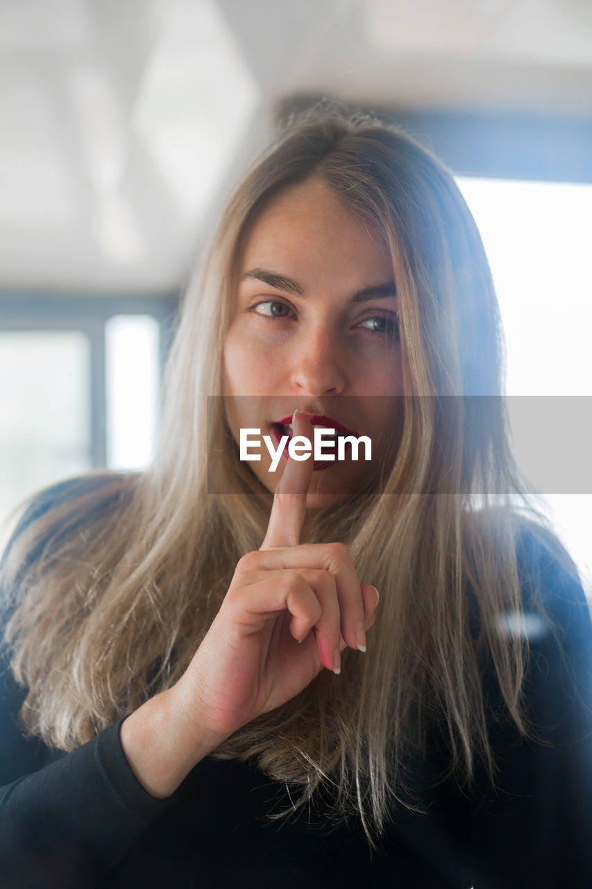 Portrait of woman with finger on lips at home