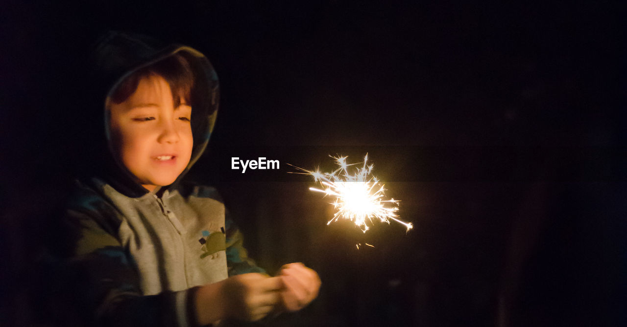Close-up of cute boy holding sparkler at night