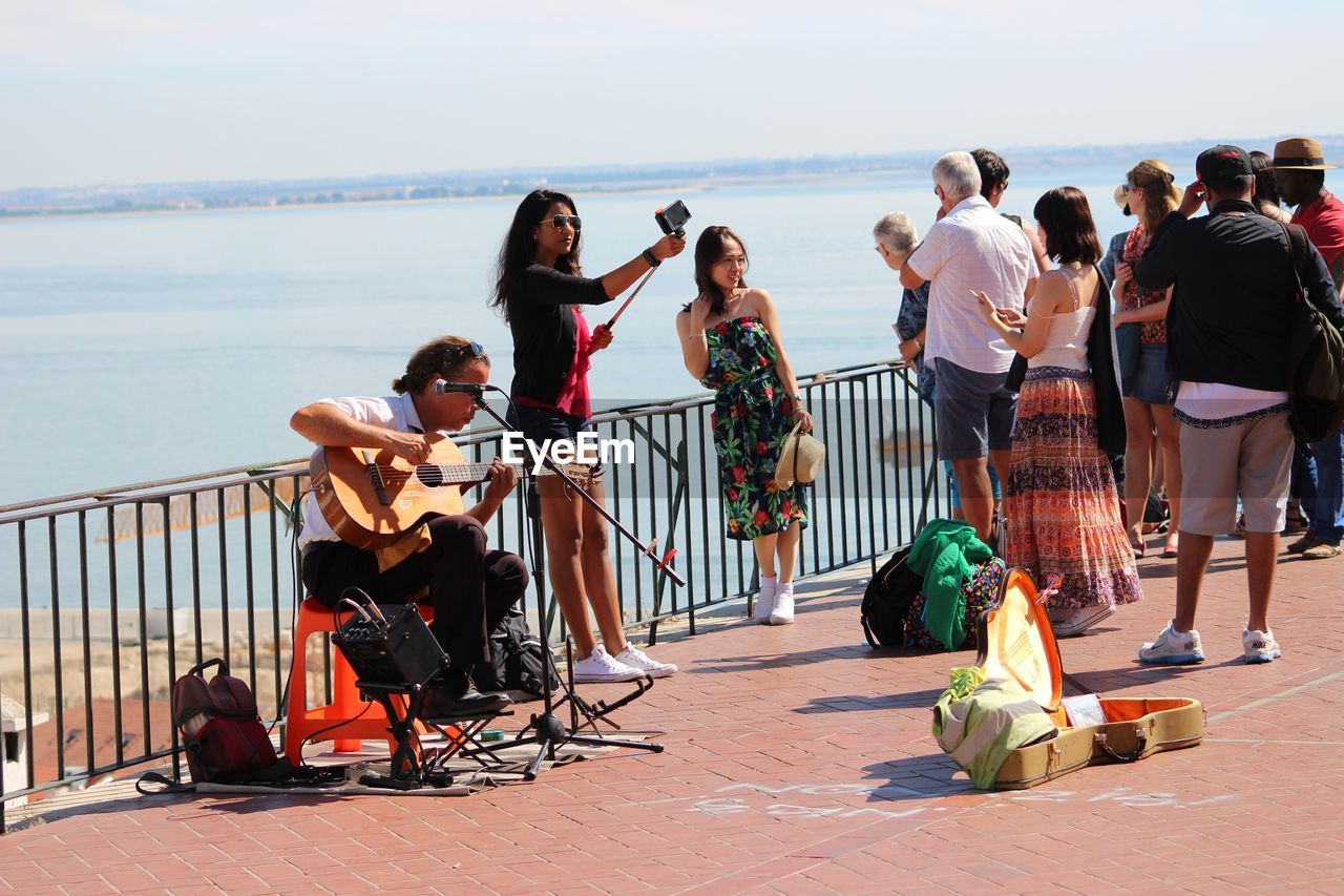 PEOPLE STANDING BY RAILING AGAINST SEA AND SKY