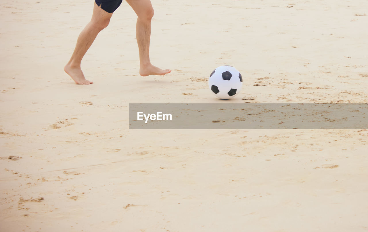 Low section of man playing with soccer ball at beach
