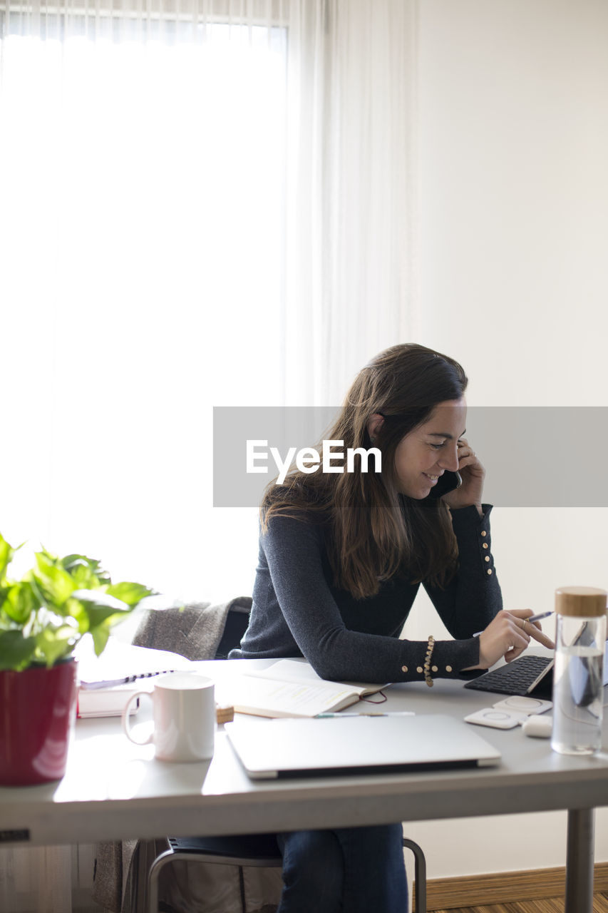 Businesswoman talking over mobile phone while sitting on table