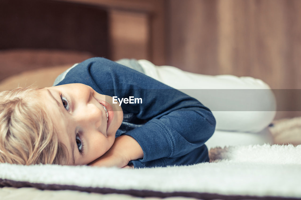 High angle portrait of cute smiling boy lying on bed at home