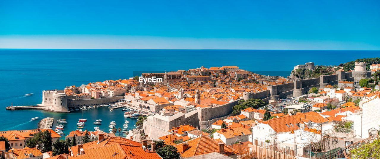 High angle view of buildings by sea against blue sky