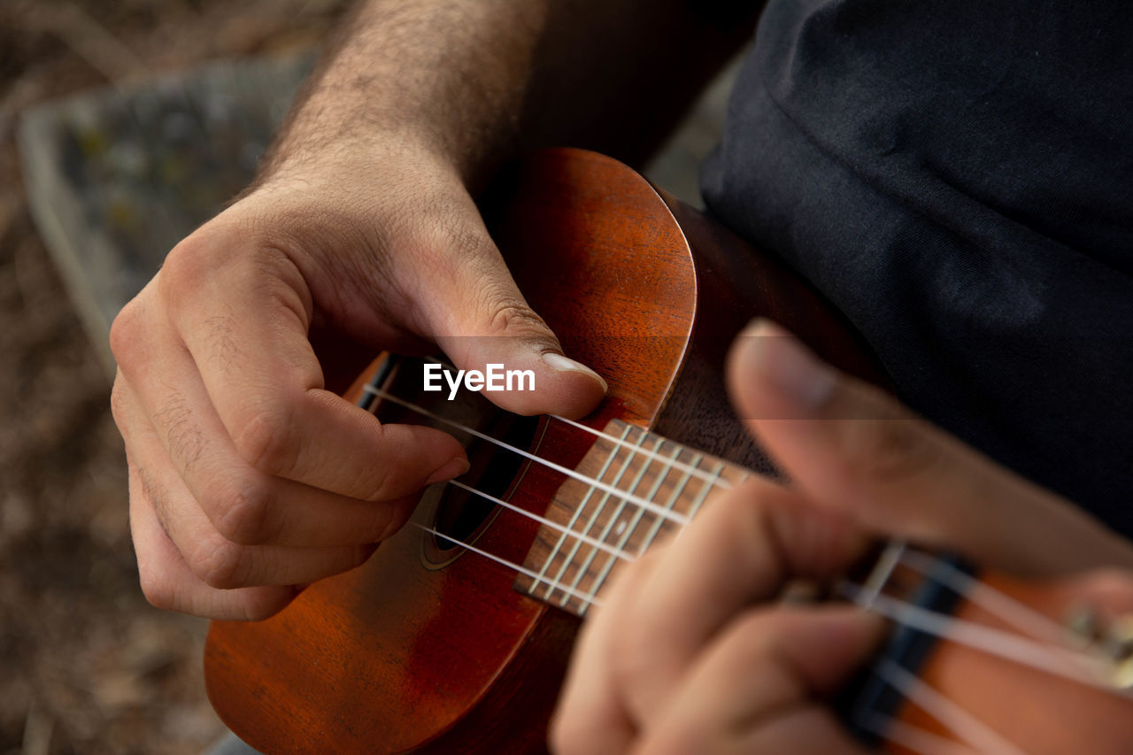 Cropped hand of man playing ukulele outdoors