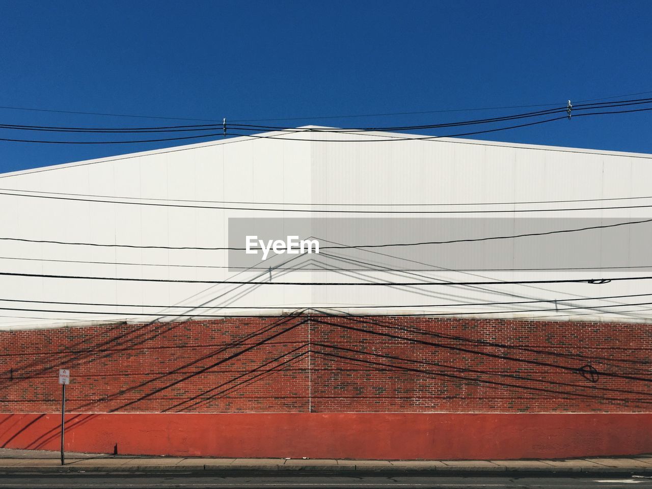 Power lines in front of factory against clear blue sky