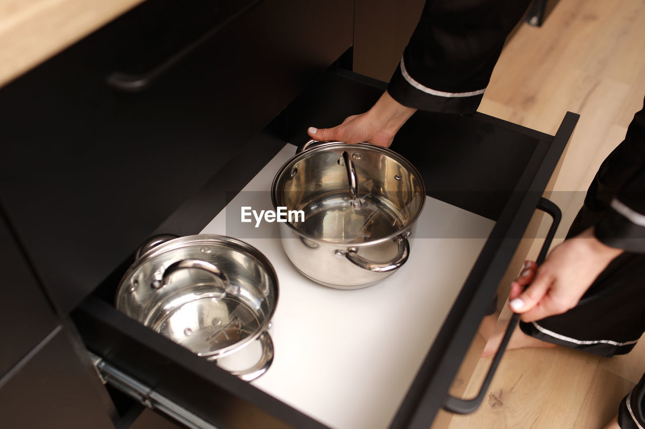 Close up of female hand pulls a new stainless steel saucepan out of the kitchen table.