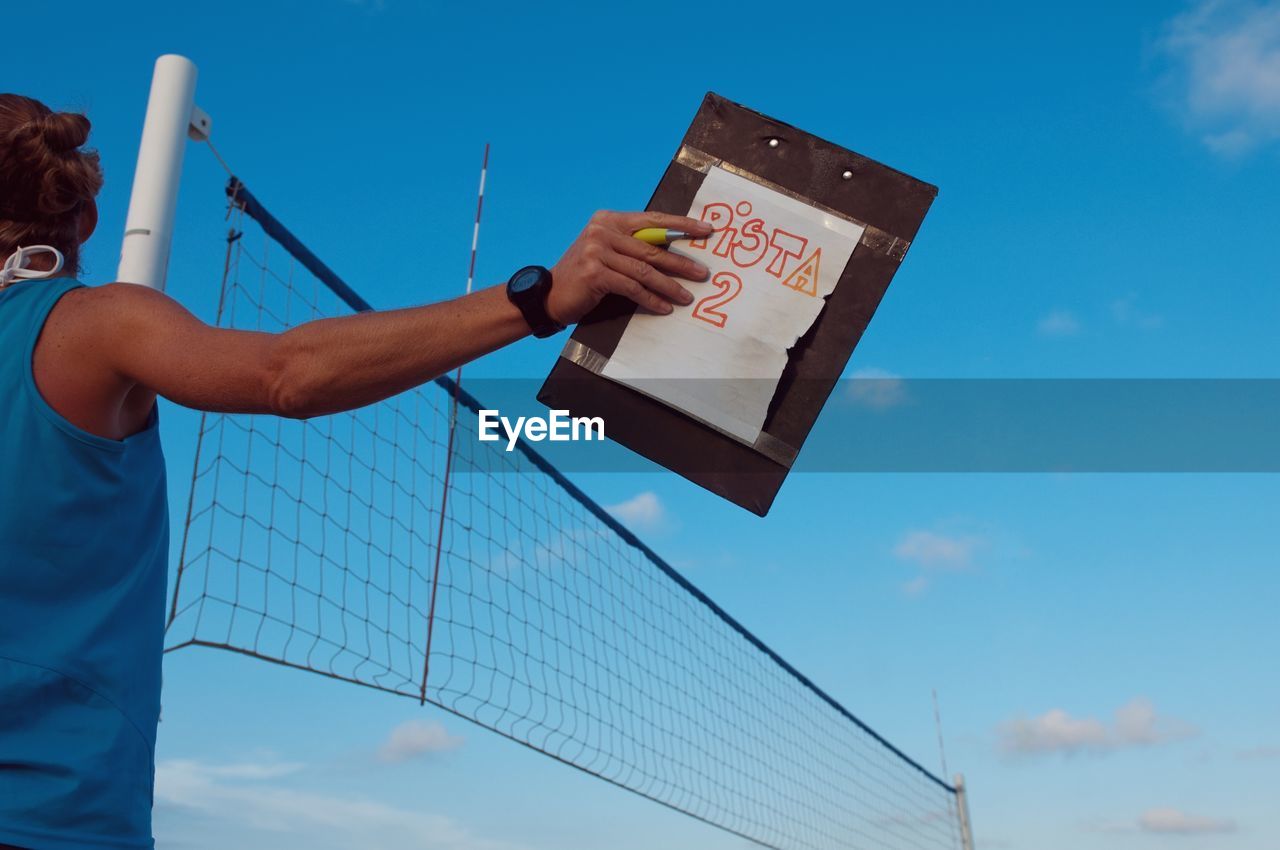 Low angle view of woman holding scorecard against blue sky