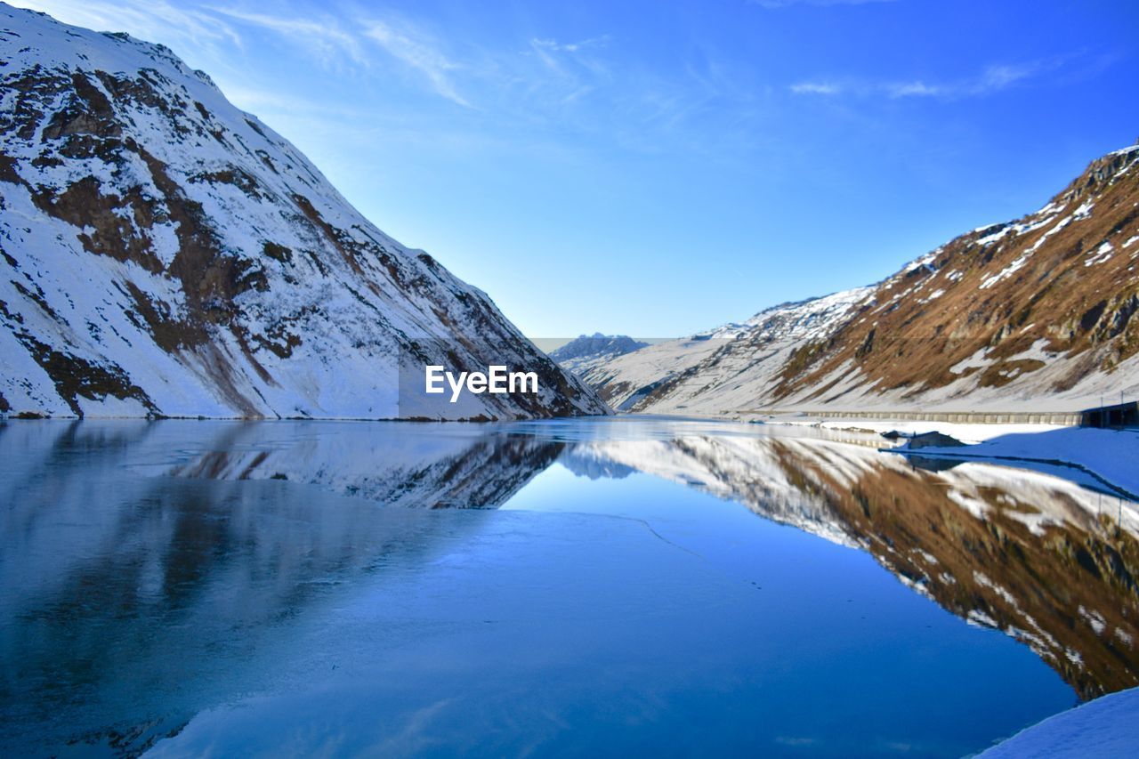 Scenic view of lake and snowcapped mountains against blue sky