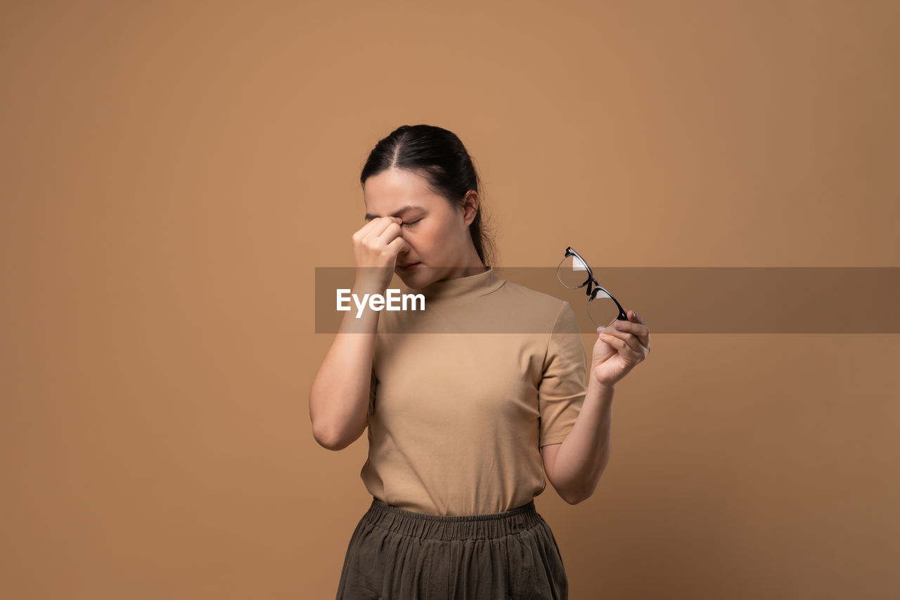 one person, studio shot, adult, colored background, indoors, photo shoot, women, holding, young adult, person, standing, portrait, copy space, hand, waist up, microphone, human face, clothing, brown hair, hairstyle, emotion, communication, eyes closed, arm, singing, female, looking, human hair