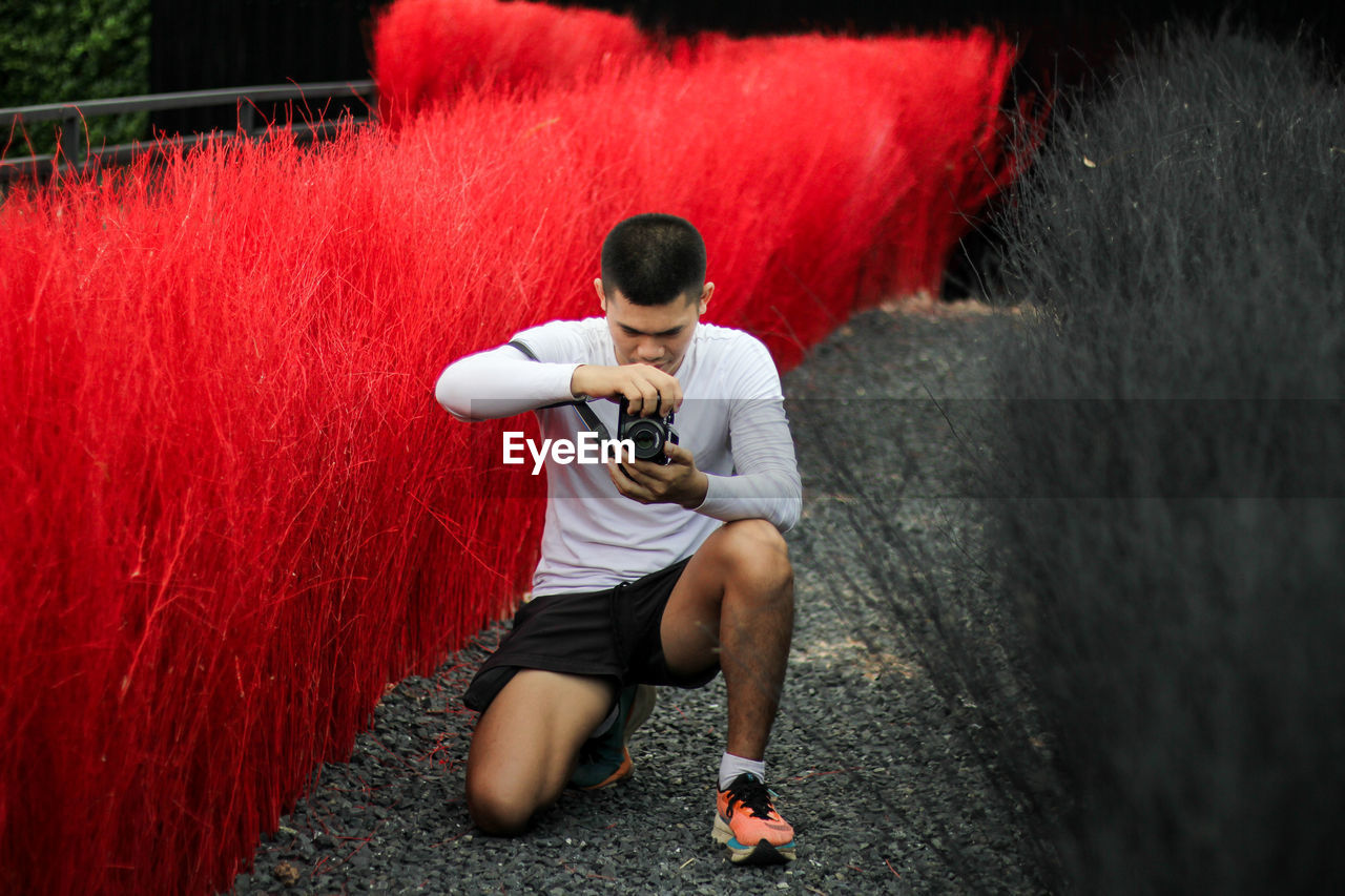 Man photographing while kneeling by plants