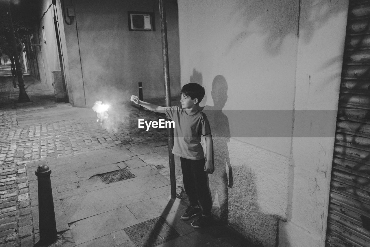 Boy holding firework while standing on footpath at night