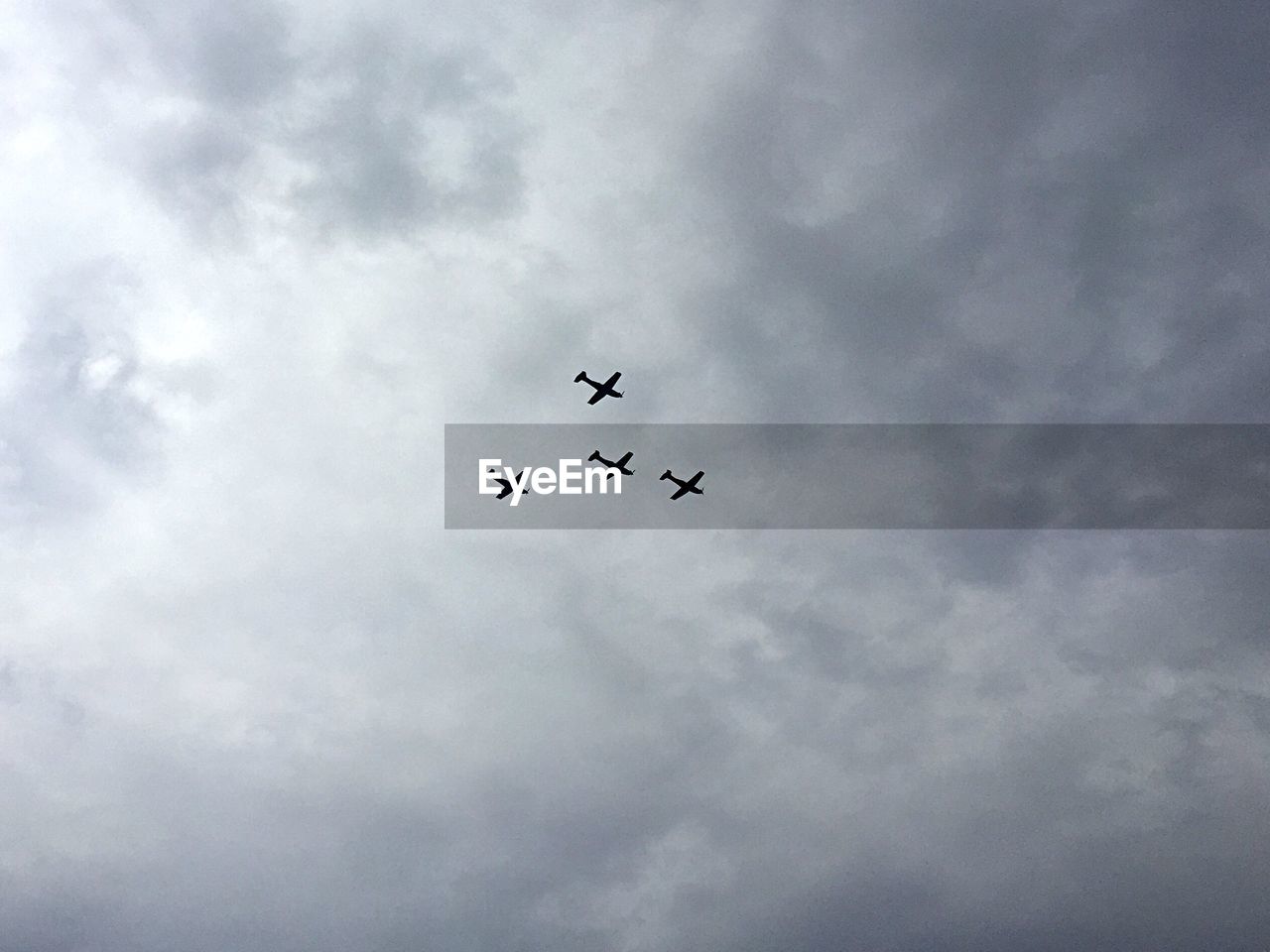 Low angle view of airplanes flying in cloudy sky