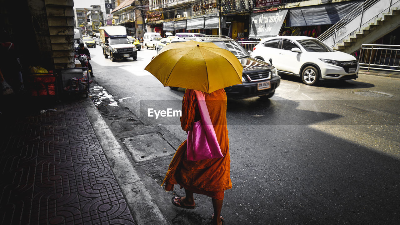 Rear view of monk walking under umbrella on street during sunny day