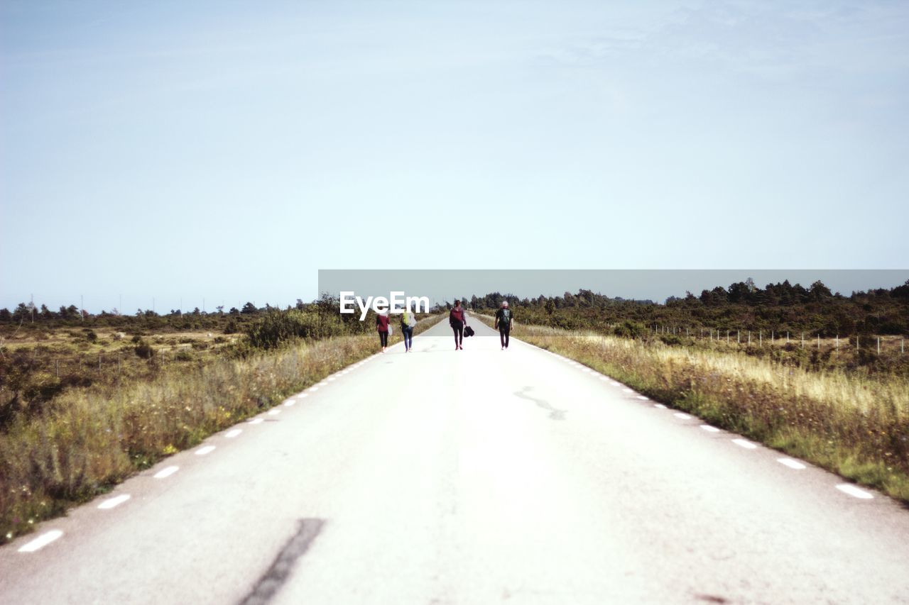 Rear view of people walking on road against sky