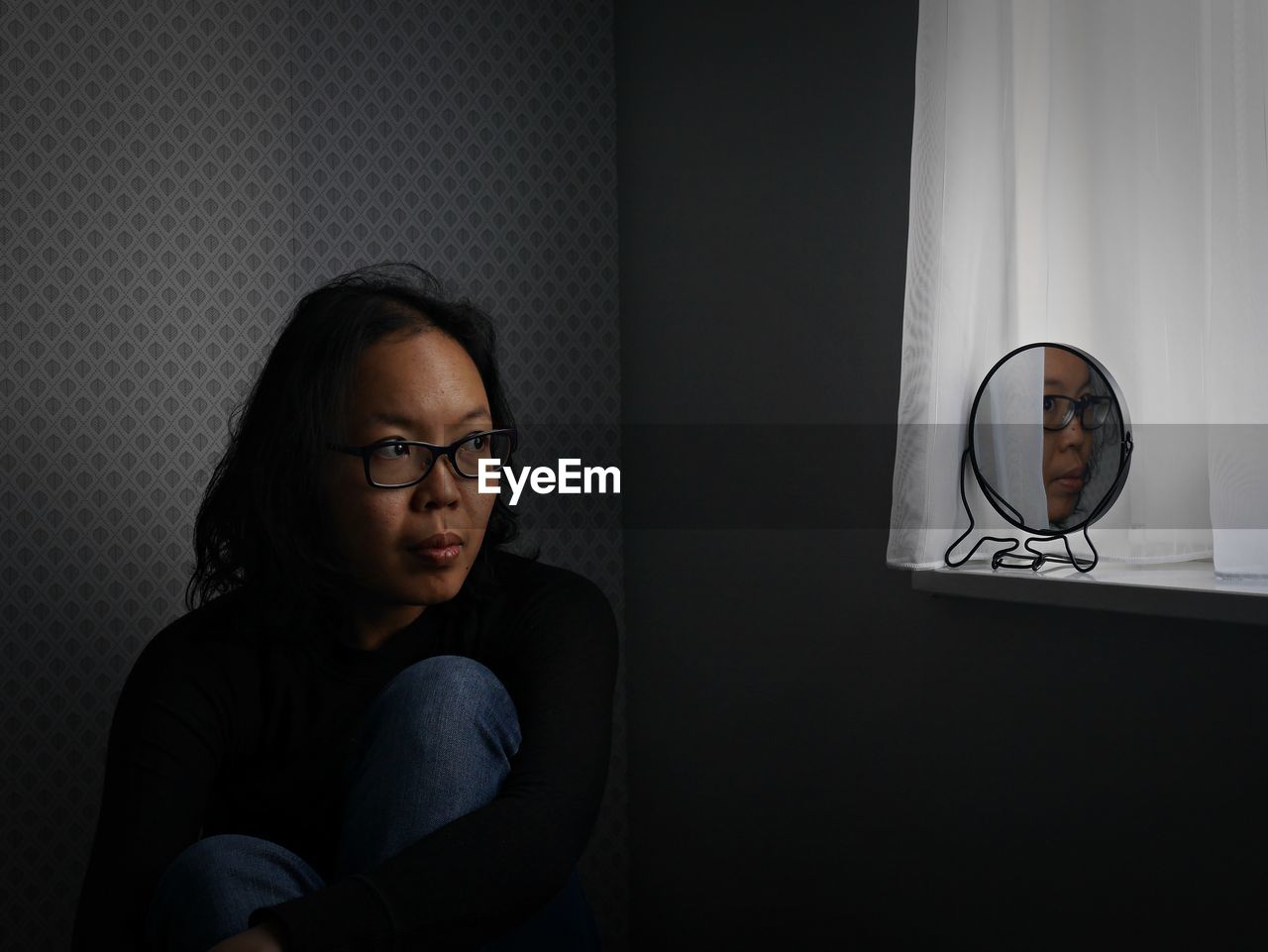 Thoughtful woman with reflection in mirror sitting at home