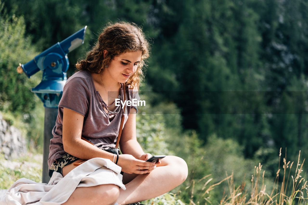 Young woman using mobile phone while sitting against tree