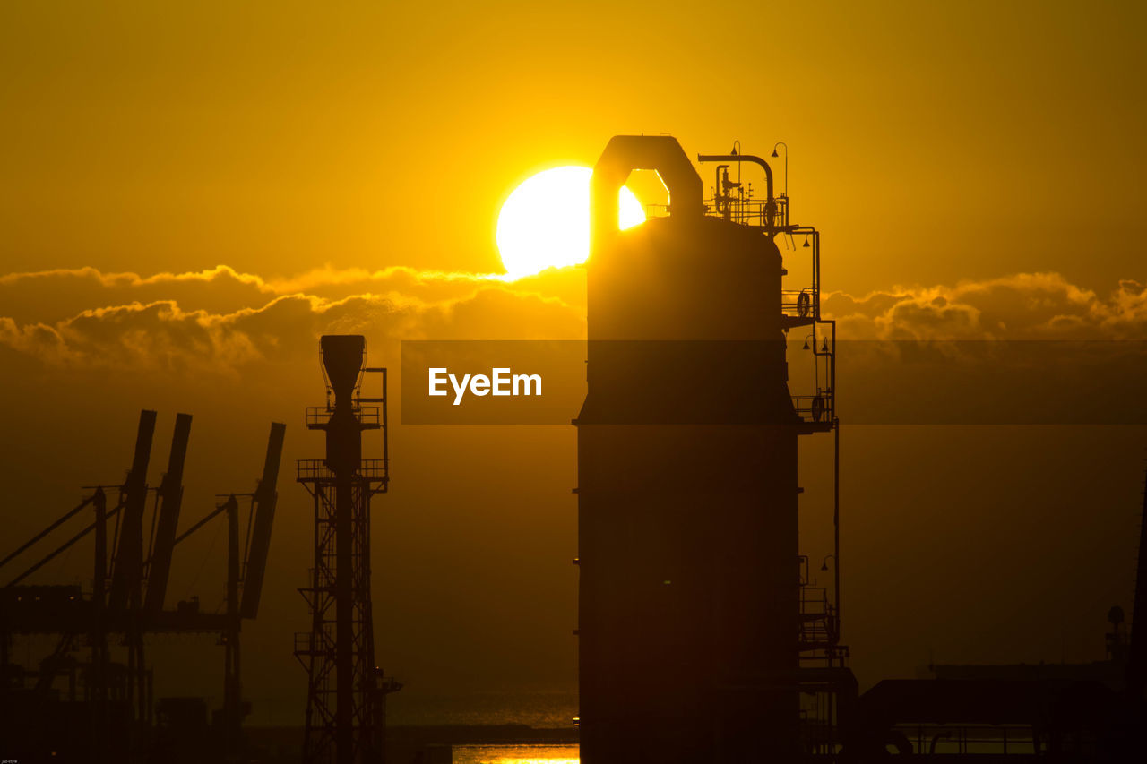 Silhouette of factory against sky during sunset