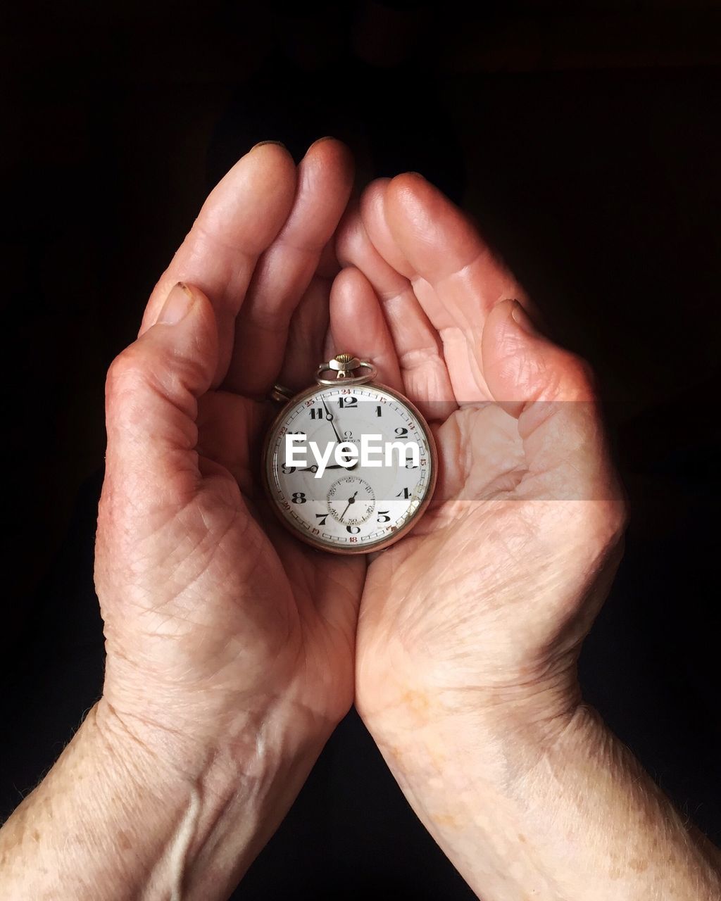 Cropped image of hand holding clock over black background