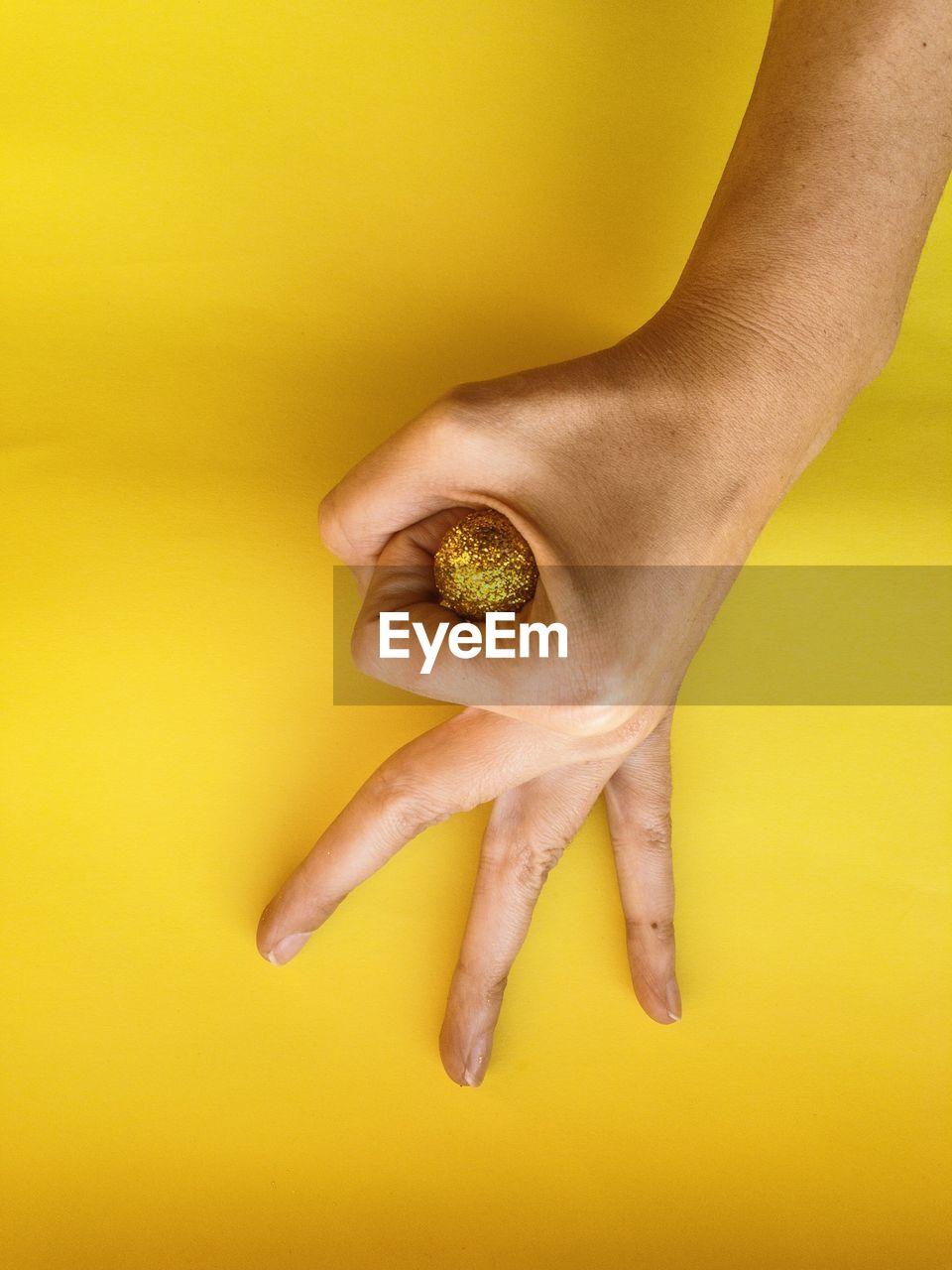 Close-up of human hand gesturing over shiny ball against yellow background