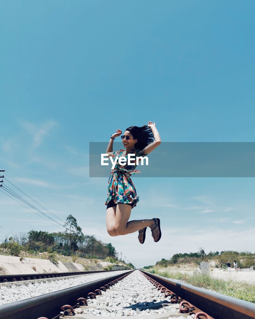 Full length of woman jumping in mid-air on railroad track against sky