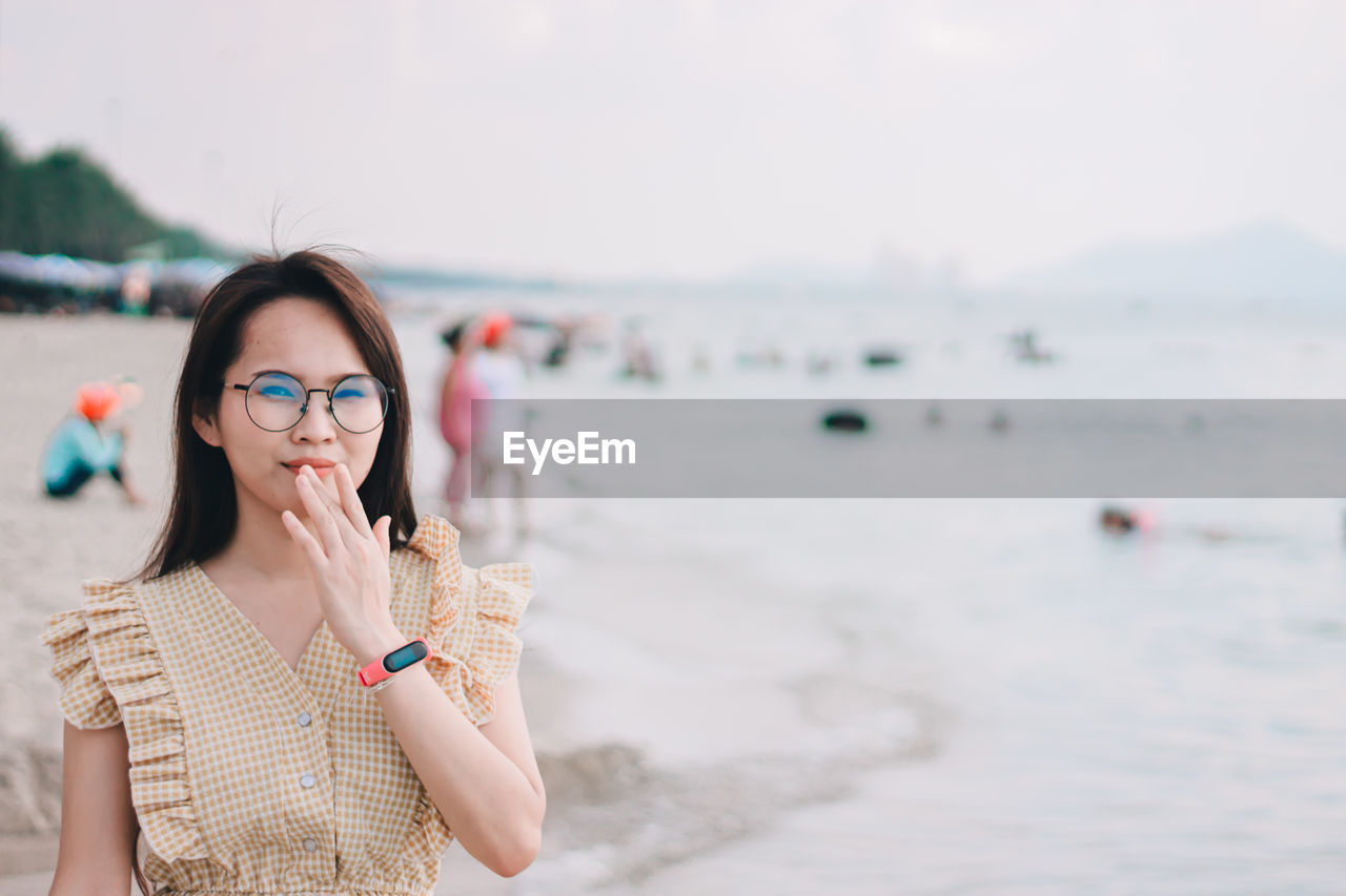 Portrait of beautiful woman wearing sunglasses gesturing while standing at beach