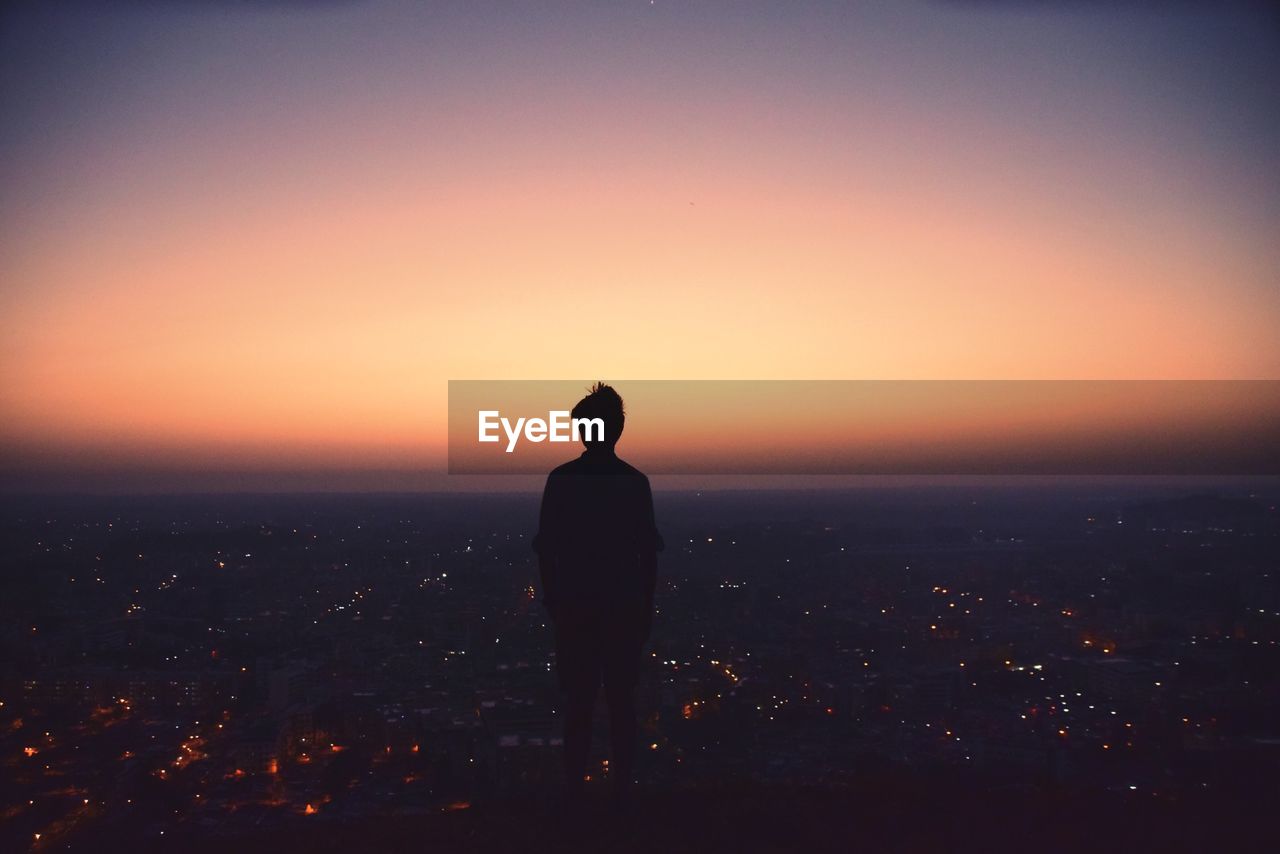 Silhouette of person looking at city view from observation point at sunrise