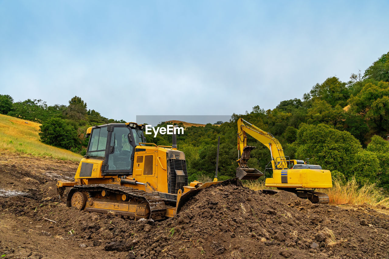 View of yellow bulldozer and excavator on plot of land. heavy equipment clears area. 