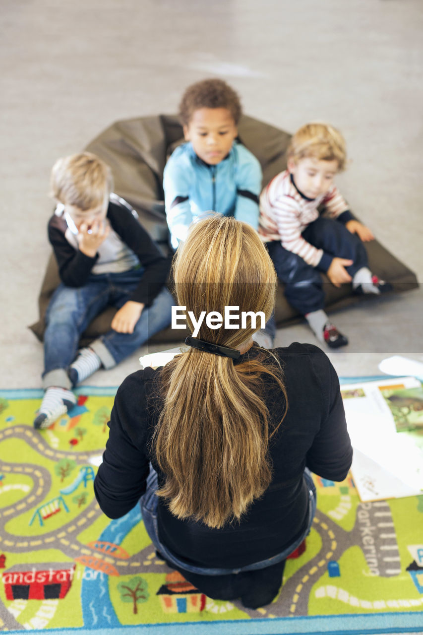 High angle view of teacher sitting in front of children at kindergarten