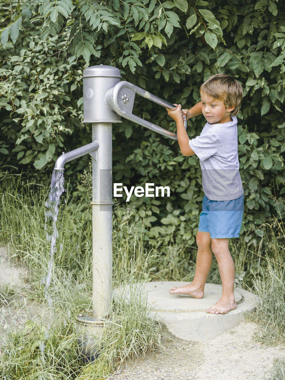 Full length of boy using water pump against plants