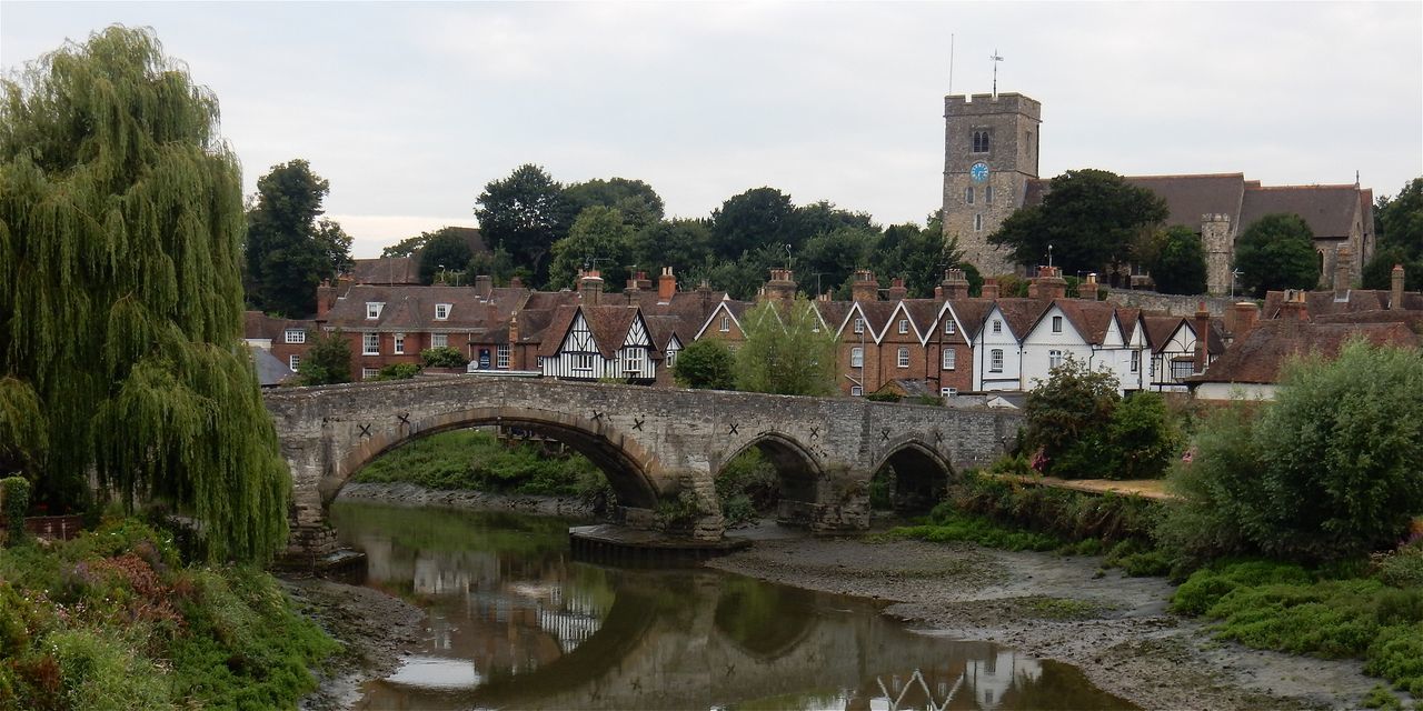Arch bridge over river by houses against sky