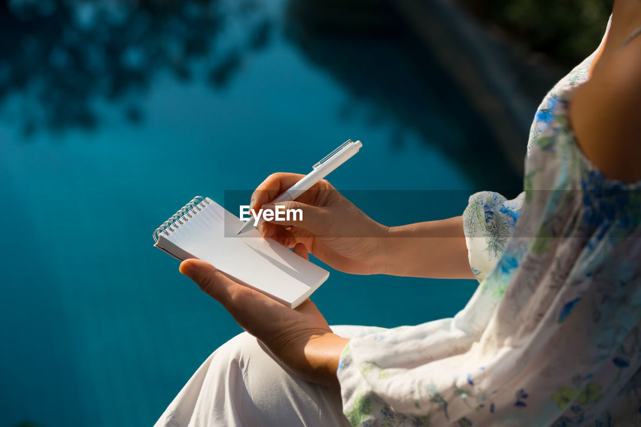 Close-up of woman writing on notepad with pencil