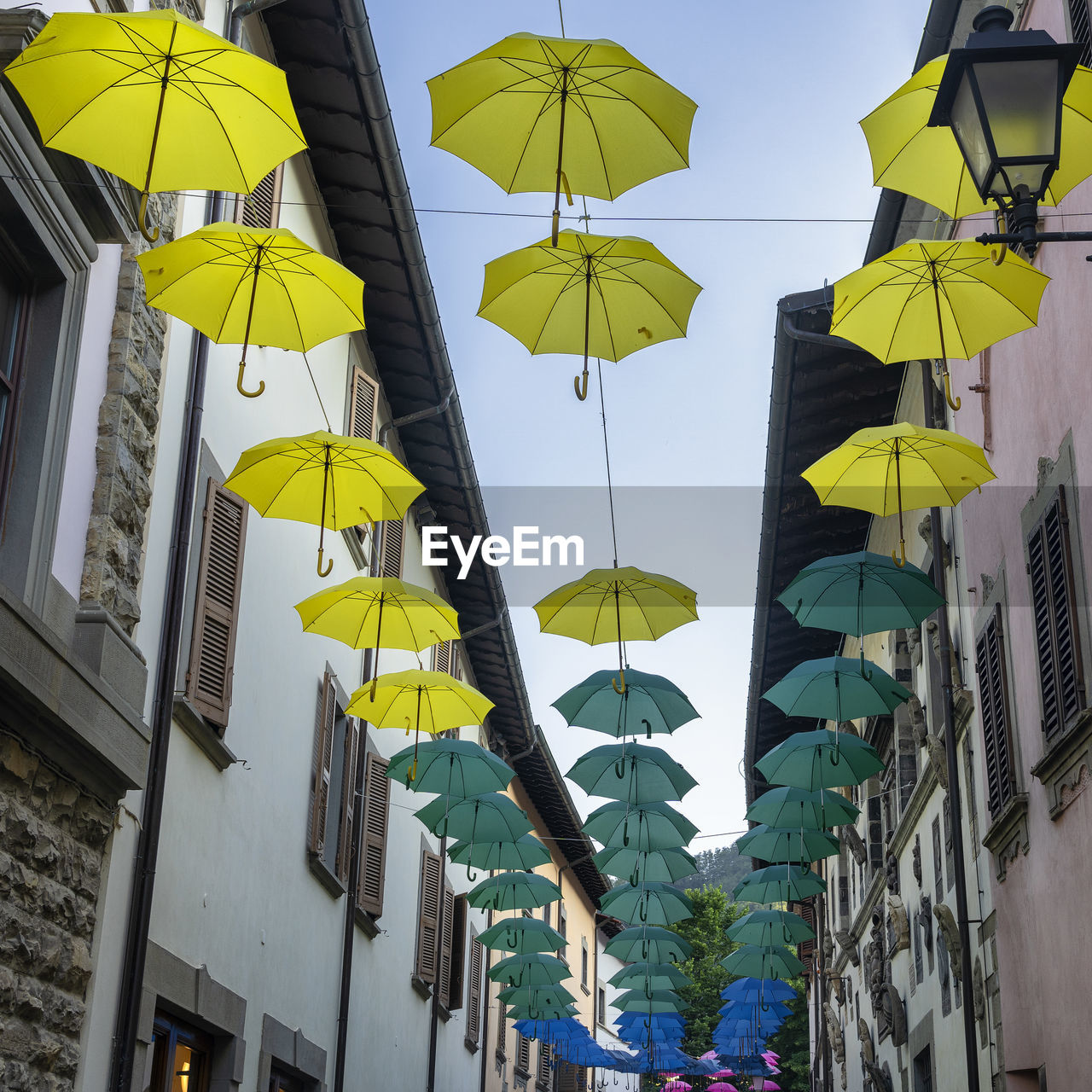 LOW ANGLE VIEW OF UMBRELLAS HANGING AGAINST BUILDINGS