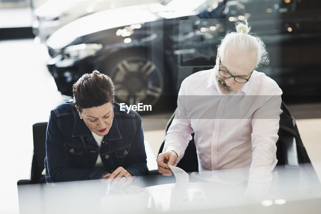 Senior man and woman reading documents while sitting at car showroom