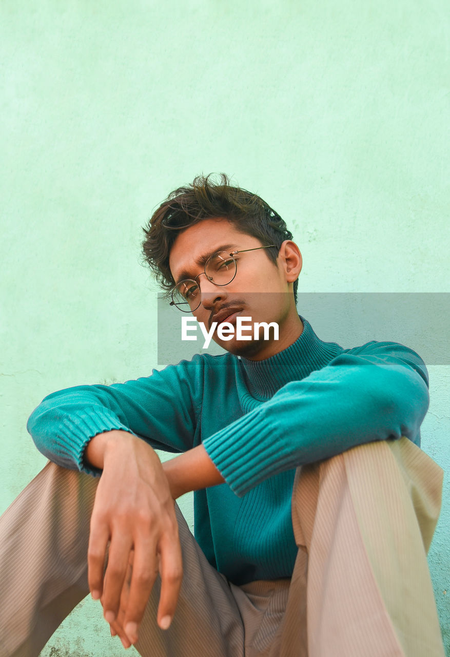 Portrait of young man sitting against wall