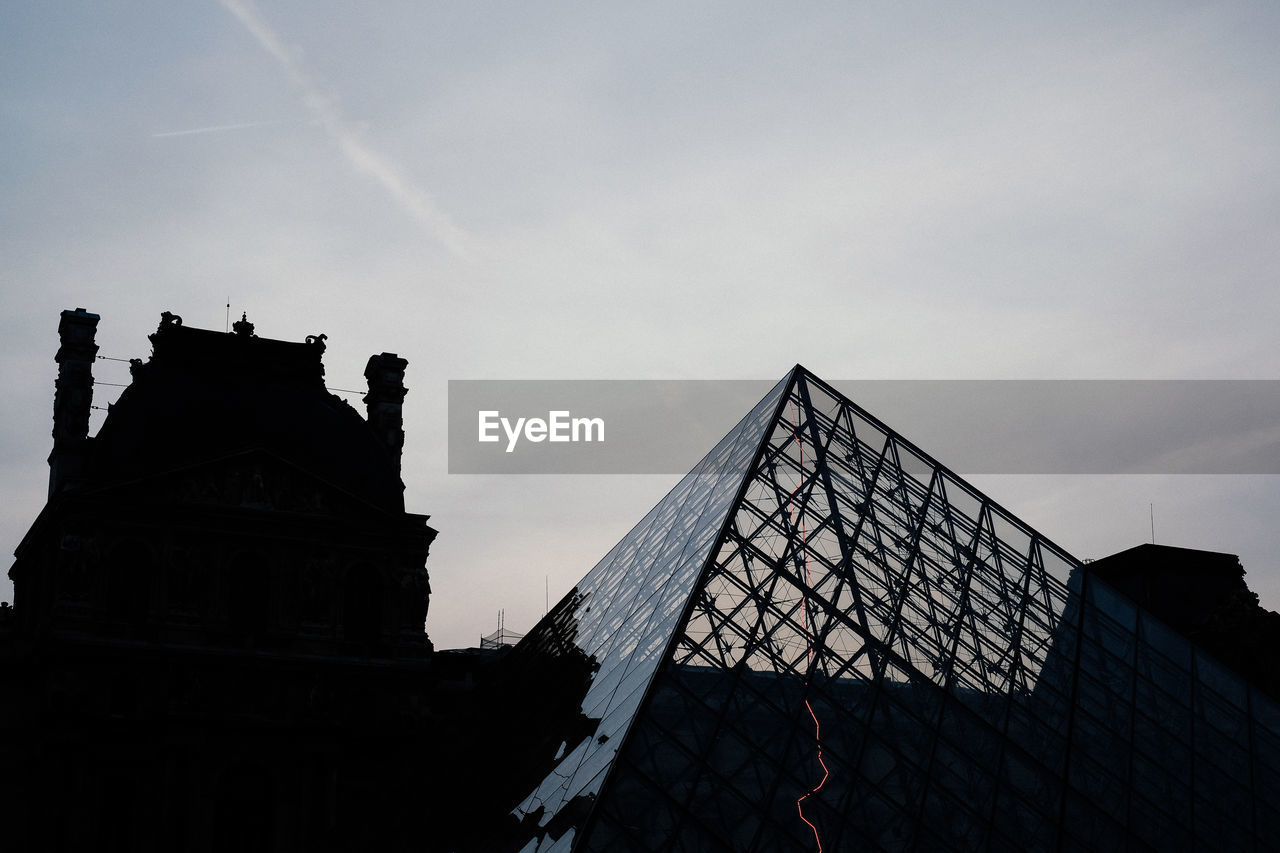 Low angle view of louvre pyramid and silhouette building against sky