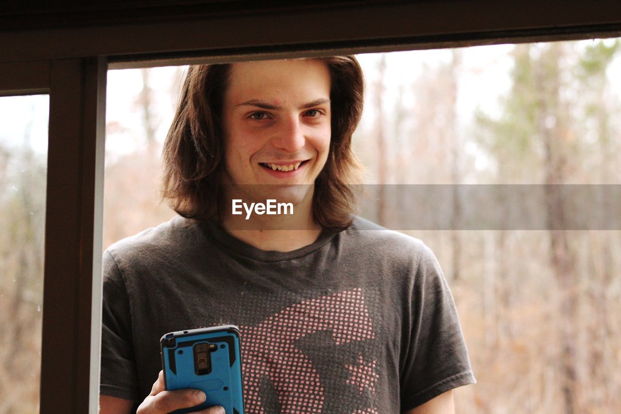 Close-up portrait of smiling young man looking through window