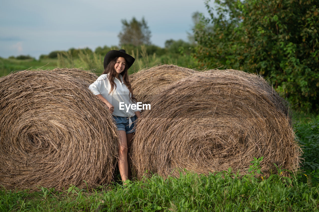 Young woman standing on field near the haystack 