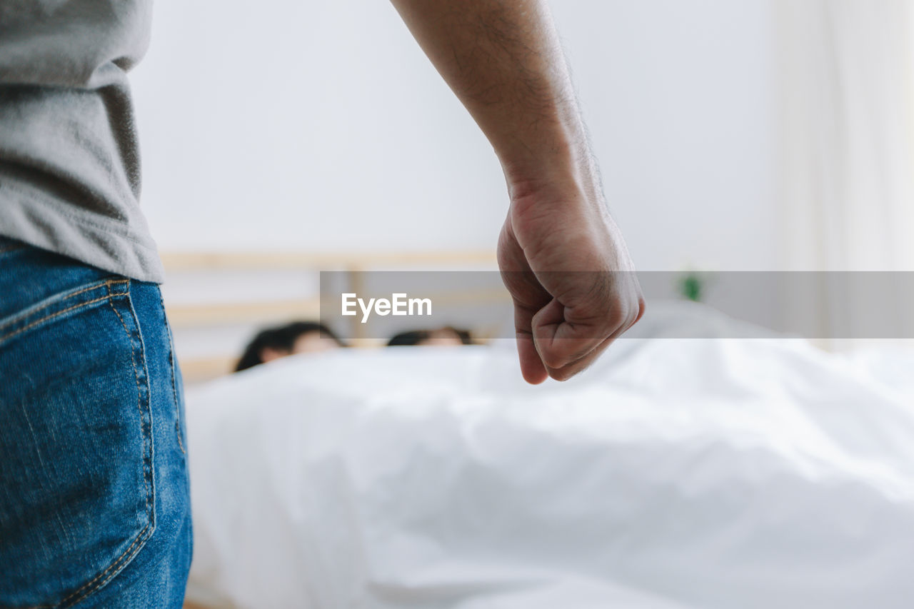 Cropped image of man clenching fist against couple sleeping on bed