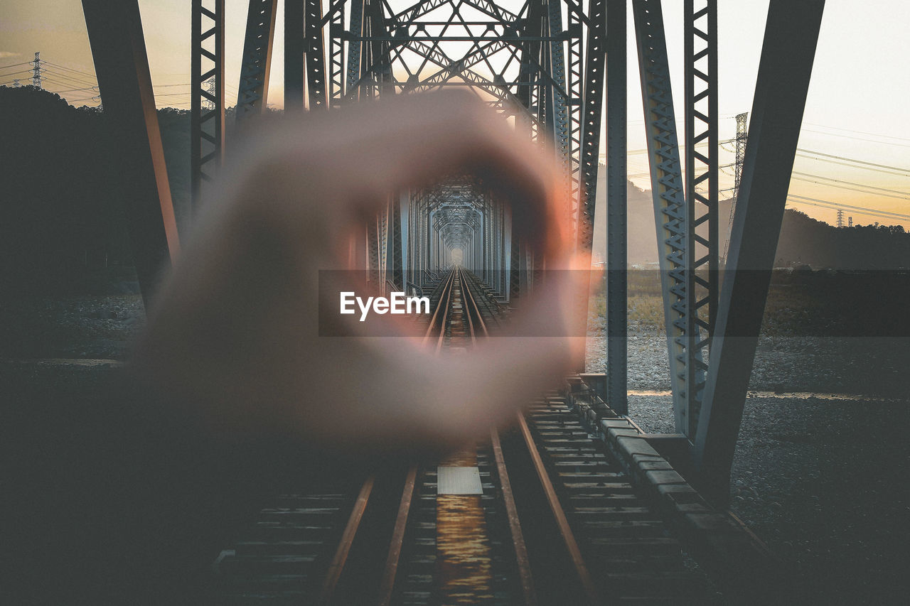 Railway bridge seen through hole made from hand against sky during sunset