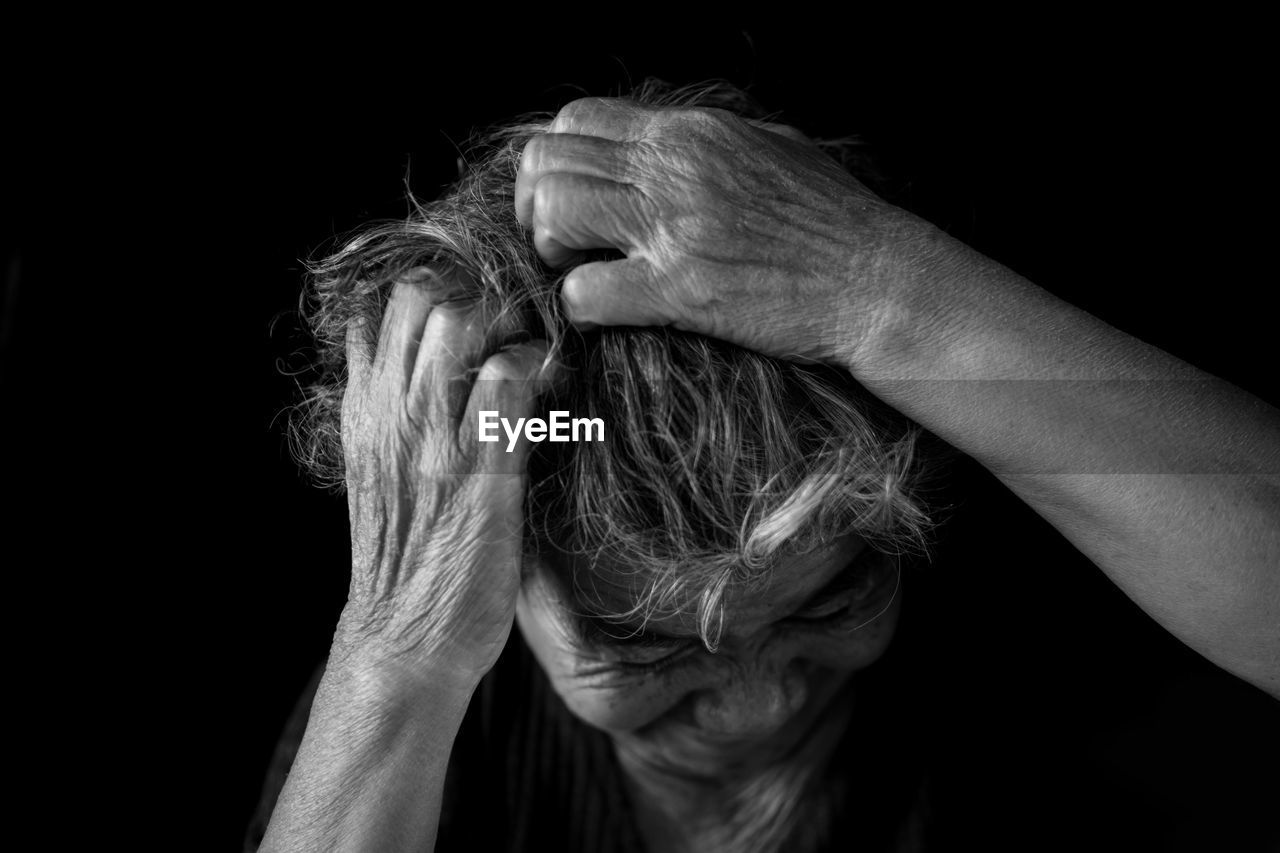 Close-up of senior woman with hands in hair against black background