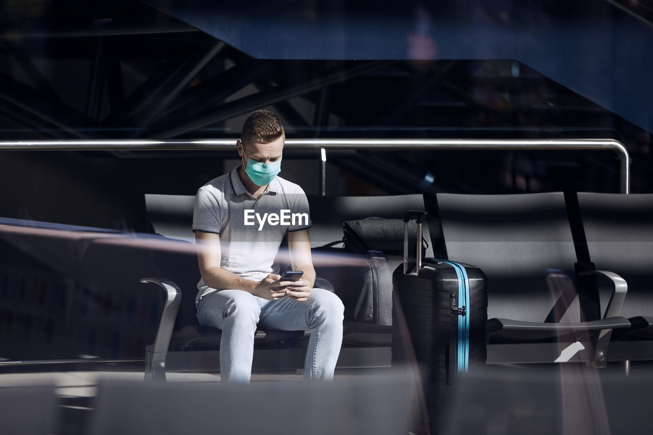 Man waiting in airport terminal and using phone. themes mobile apps and travel in new normal.